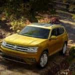Yellow Volkswagen Atlas parked on a shadowy road near trees and shrubbery