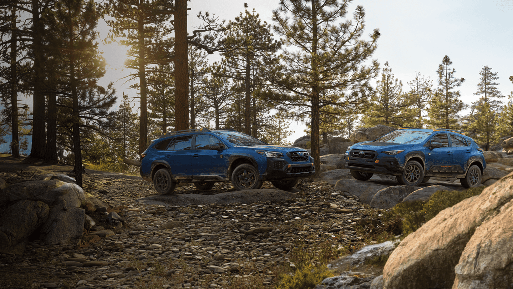 A blue silver Subaru is parked next to a lake with two kayaks nearby