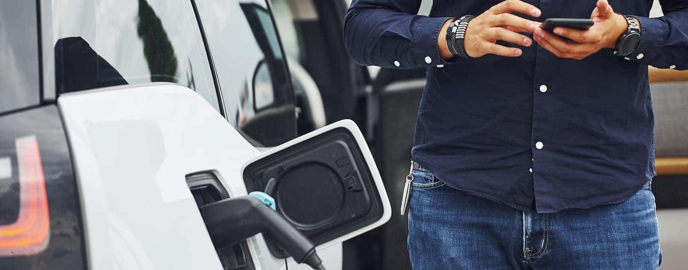 A close up shows a man holding a phone while waiting for his Chevy EV to charge.