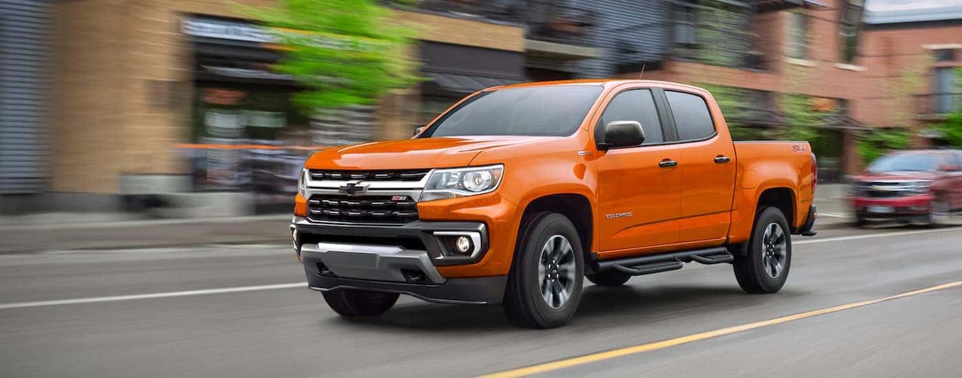 An orange 2021 Chevy Colorado is driving on a city street after leaving an Indiana Chevy dealership.