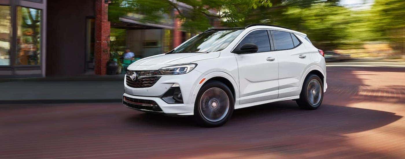 A white 2021 Buick Encore GX is driving on a brick road downtown.