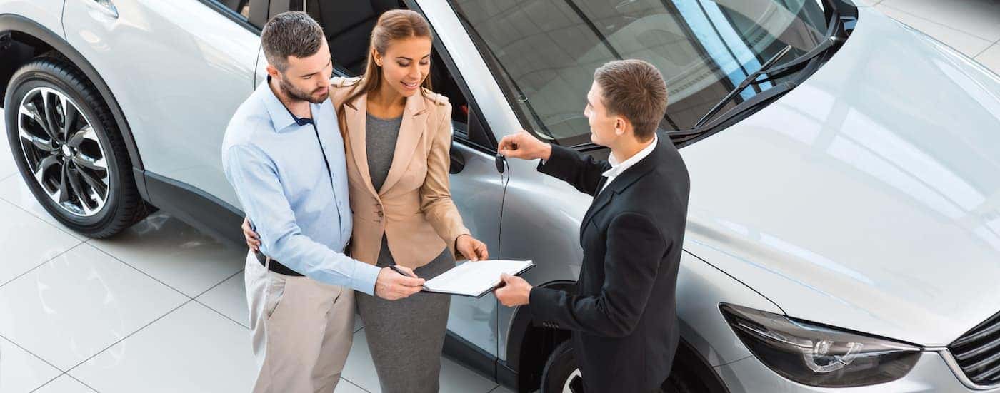 A salesman is going over financing with a couple in front of a silver SUV.