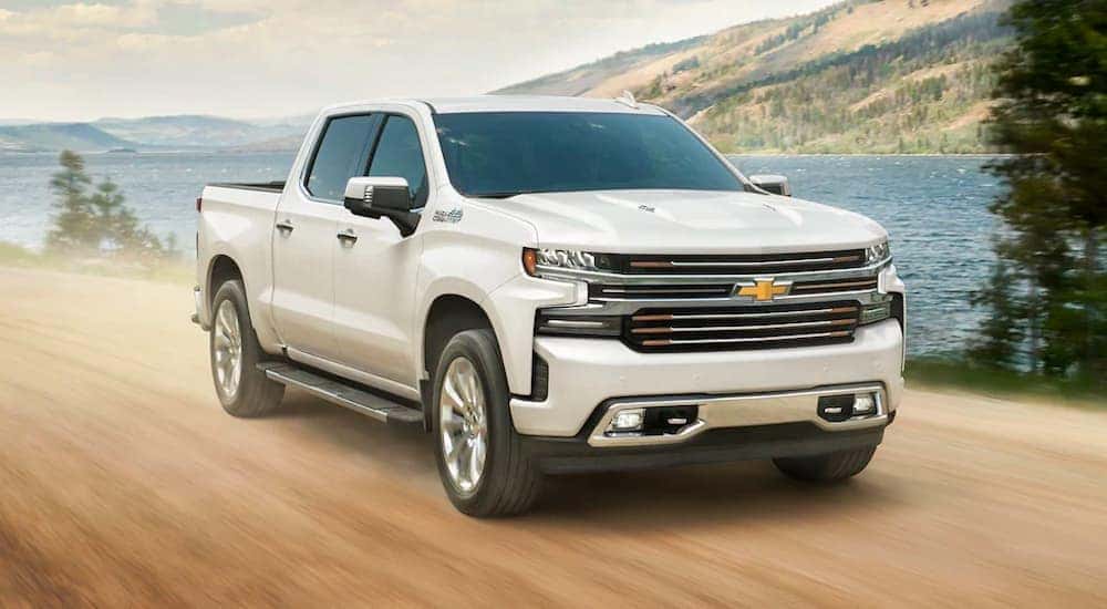 A white 2021 Chevy Silverado is shown driving on a dirt road past a river.