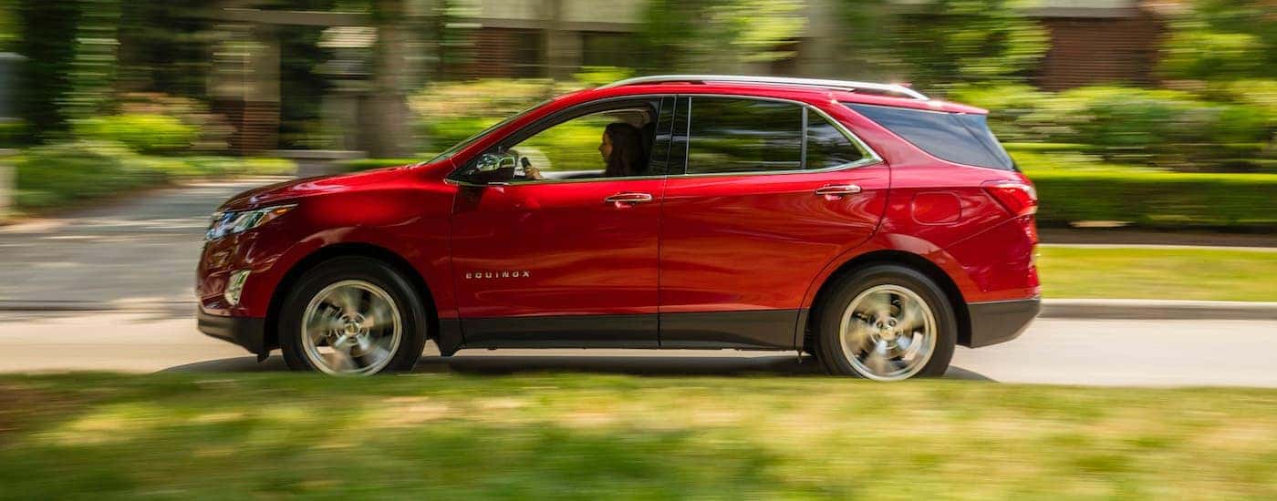 A red 2018 Chevy Equinox is shown from the side driving on a road past grass.