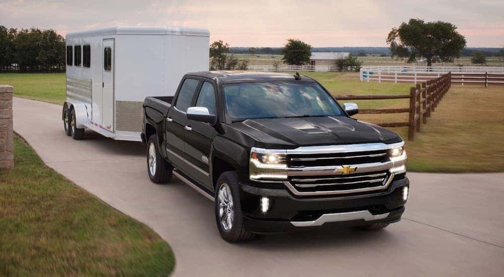 A black 2018 Chevy Silverado 1500 is towing a white enclosed trailer out of a farm.