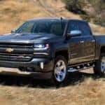 A grey 2018 Chevy Silverado 1500 from a used Chevy dealer is driving on a dirt path.