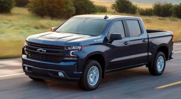 A dark blue 2019 Chevy Silverado is driving past grass after leaving a used Chevy dealer.