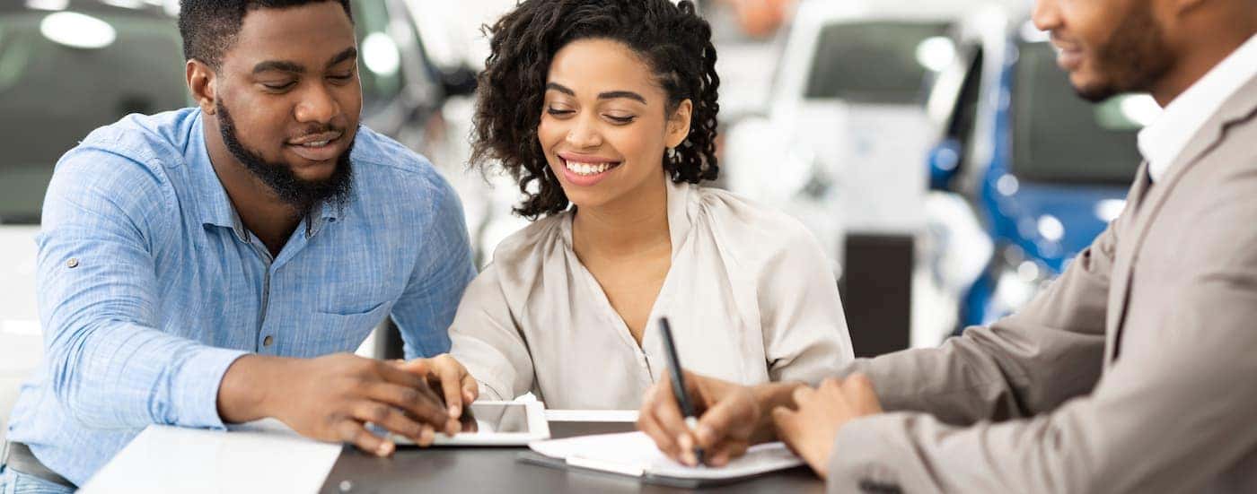 A couple is signing paperwork with a salesperson at a dealer.