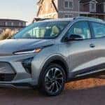 A new Chevy EV, a silver 2022 Chevy Bolt EUV, is parked in front of a house at sunset.