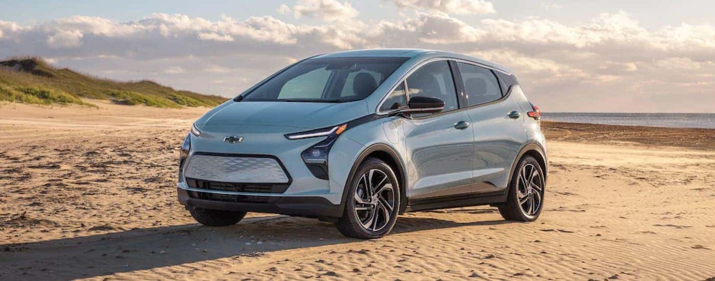 A blue 2022 Chevy Bolt EV is shown from the side parked on a beach