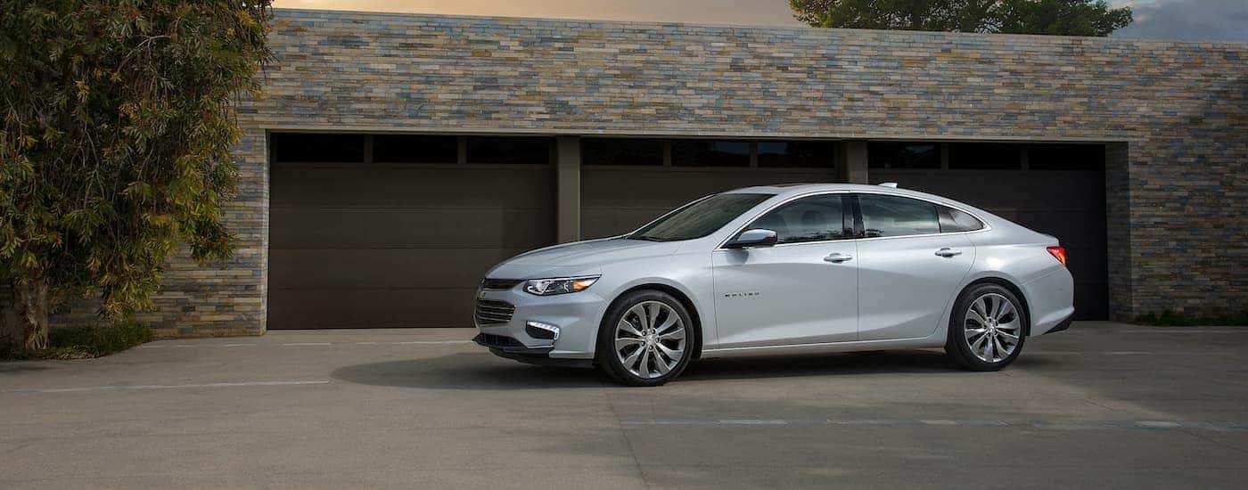 A silver 2017 Chevy Malibu is shown from the side parked in front of a garage.