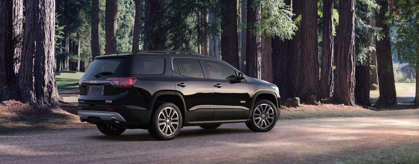 A black 2018 GMC Acadia is parked on a dirt road in front of trees.
