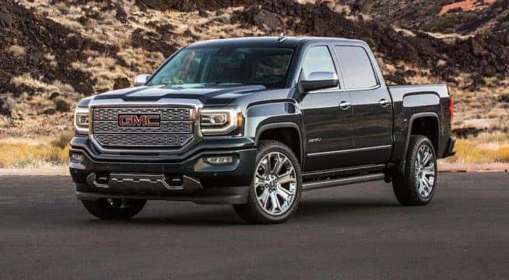 A black 2018 GMC Sierra 1500 is parked in front of sandy hills with shrubs.