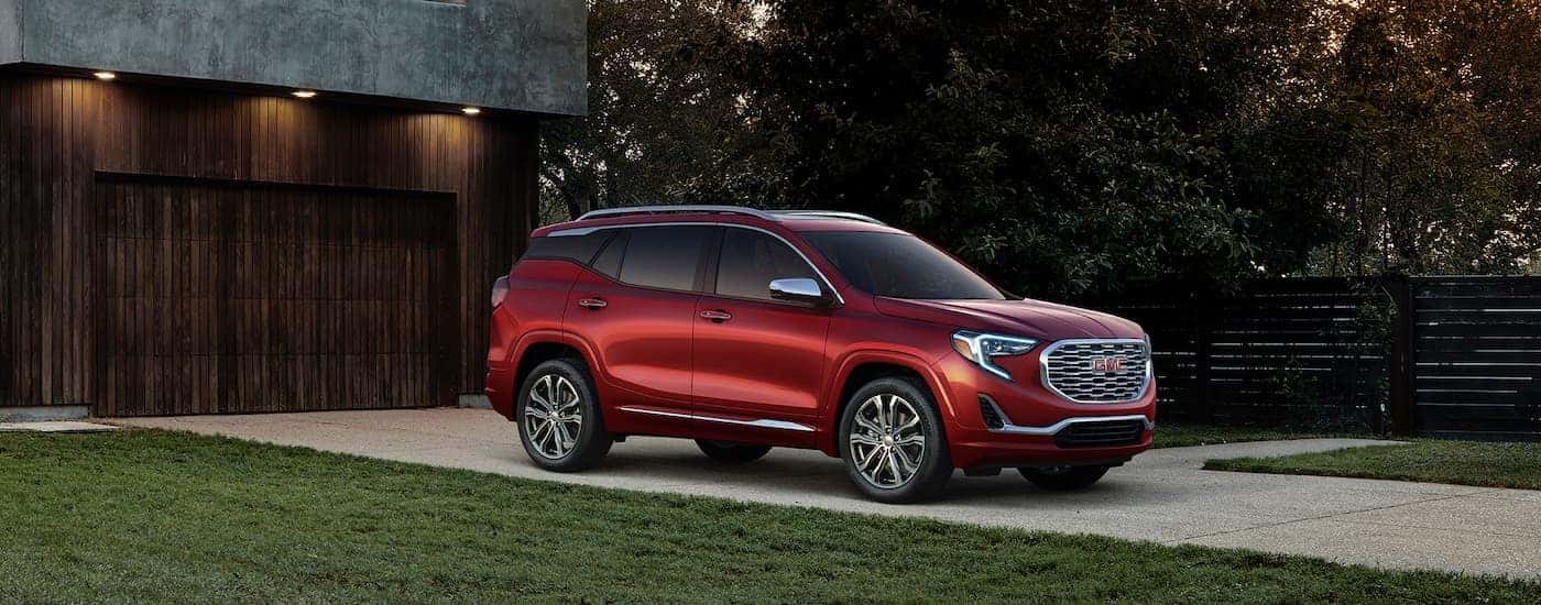 A red 2018 GMC Terrain Denali is parked in front of a modern house after leaving a used GMC dealer.