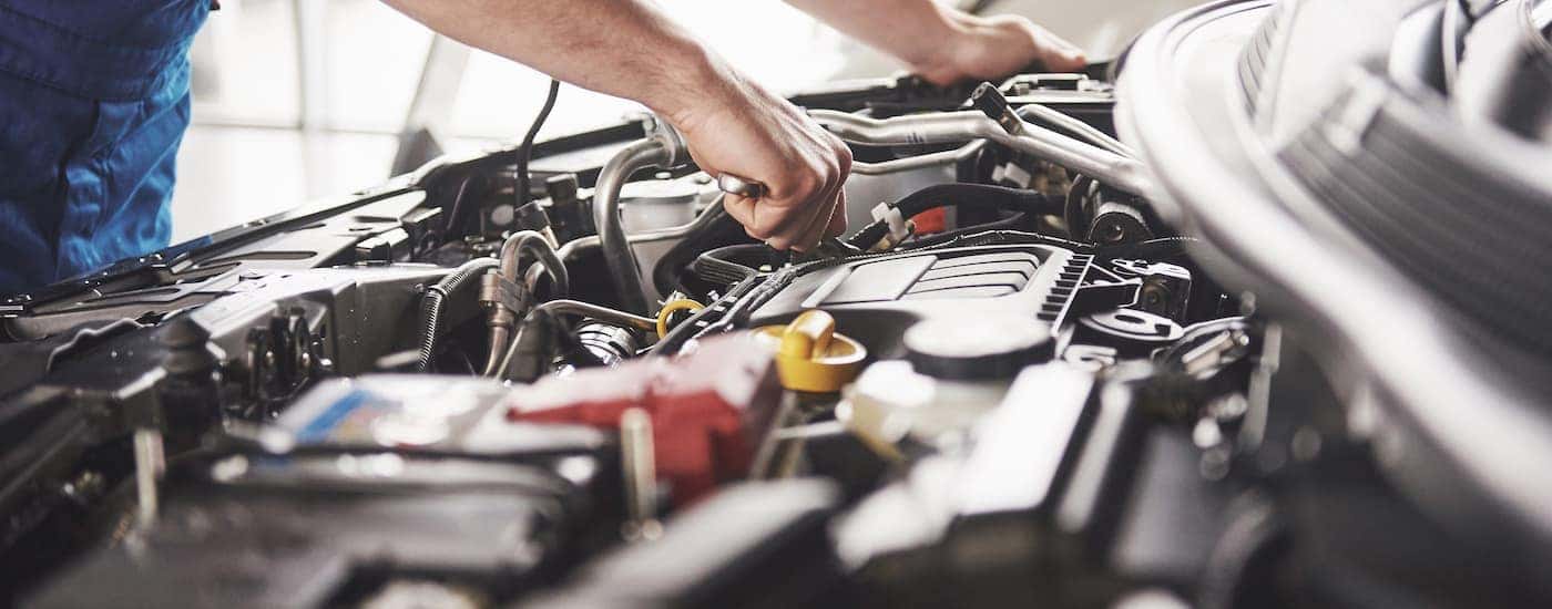 A mechanic is shown working under the hood of a vehicle in a closeup.