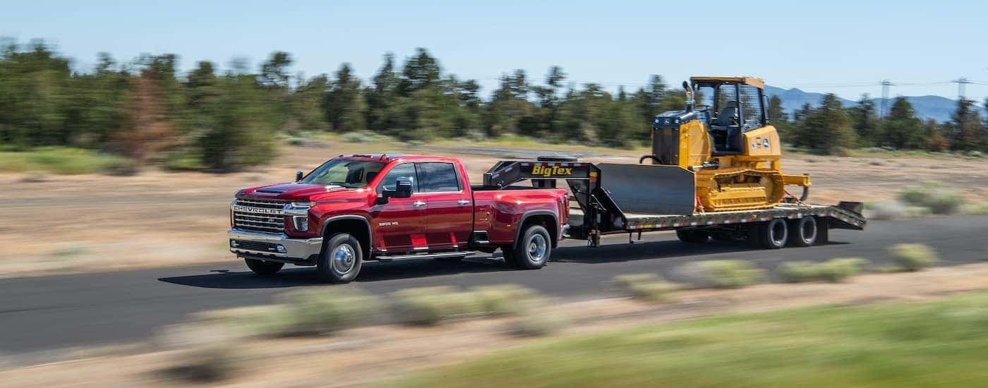 A red 2021 Chevy Silverado 3500 HD is shown from the side towing a gooseneck trailer with construction equipment.