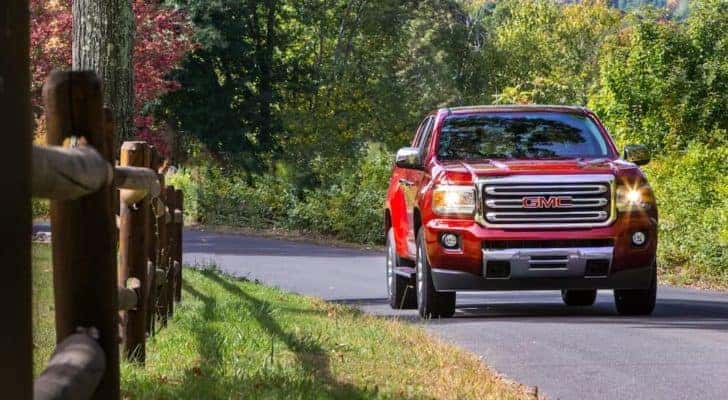 A red 2018 GMC Canyon SLT Diesel is shown from the front driving past a fence.