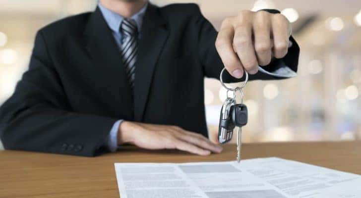 A salesman is holding out a set of keys at a used car dealer in Louisville.