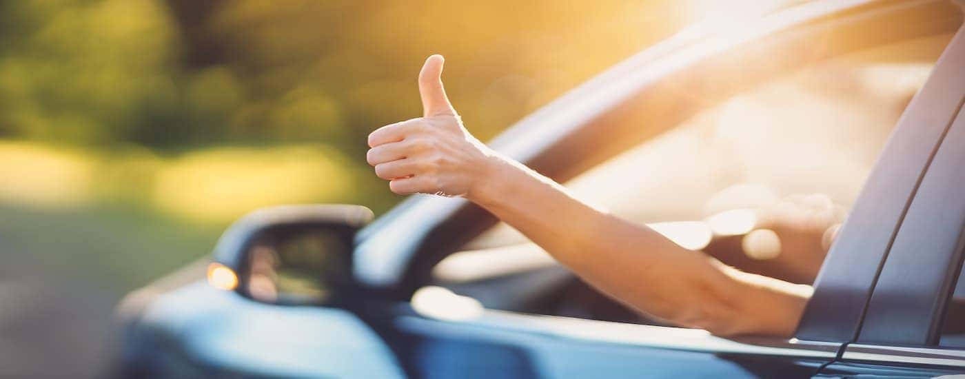 A man is holding a thumbs up out of a car window.