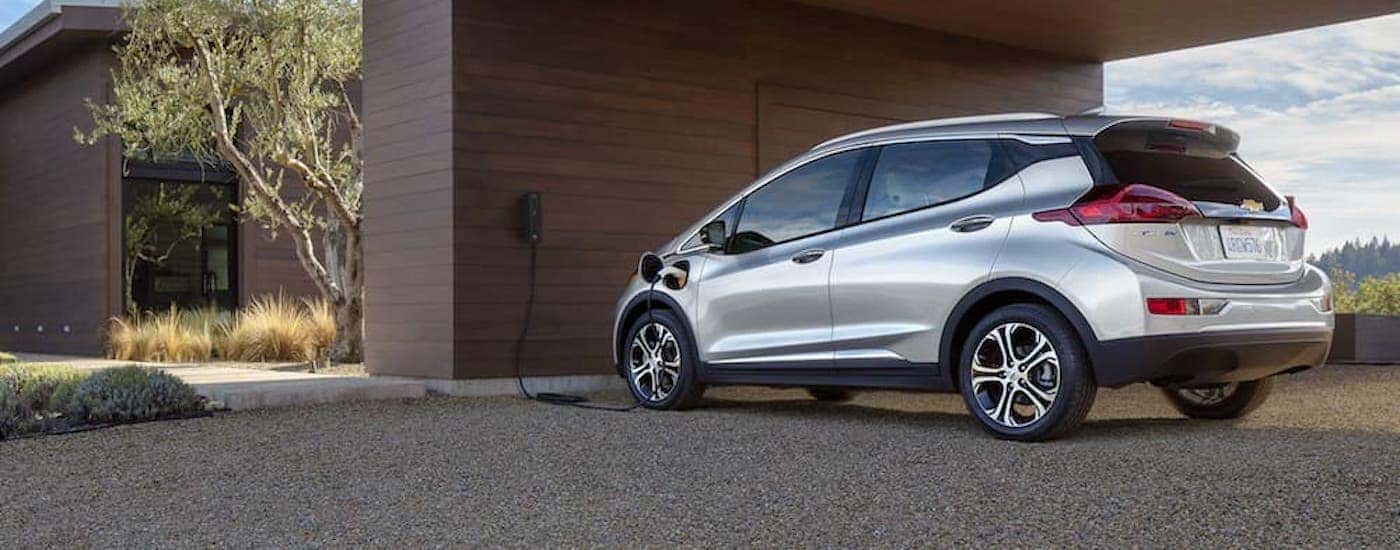 A silver 2020 Chevy Bolt EV is charging at a modern home.