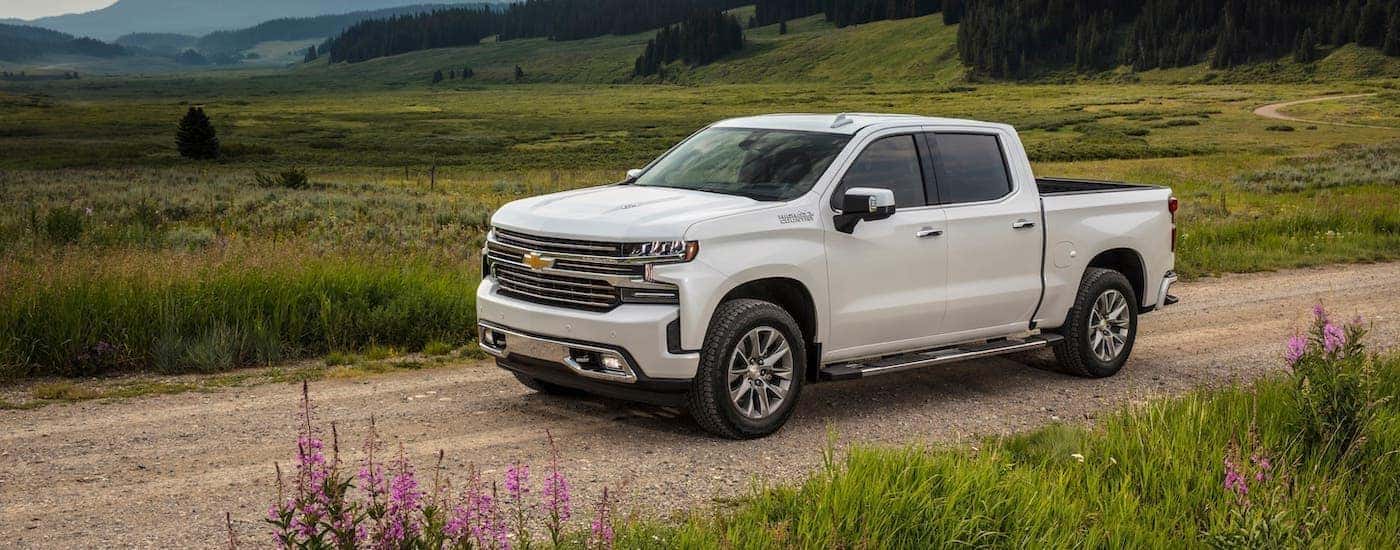 A white 2020 Chevy Silverado 1500 is parked on a dirt road overlooking a field and mountain.