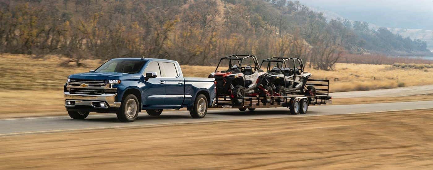 A blue 2020 Chevy Silverado is towing two side by sides on an open trailer.