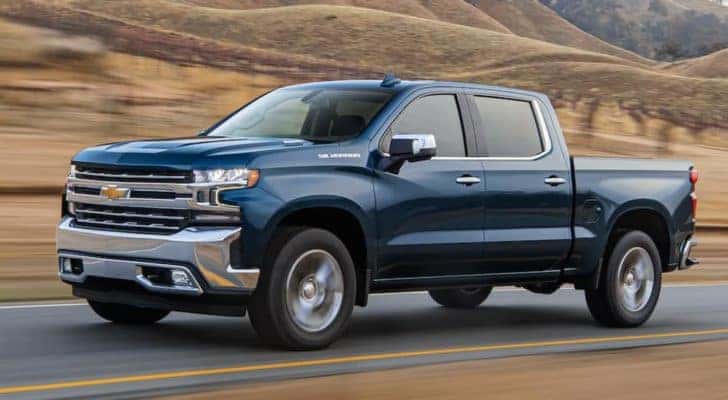 A blue 2020 Chevy Silverado 1500 is driving on a road past a vineyard after leaving a used truck dealership.