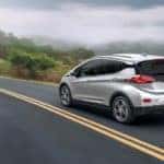 A silver 2020 Chevy Bolt EV is driving down a two way road after leaving a used Chevy dealership.