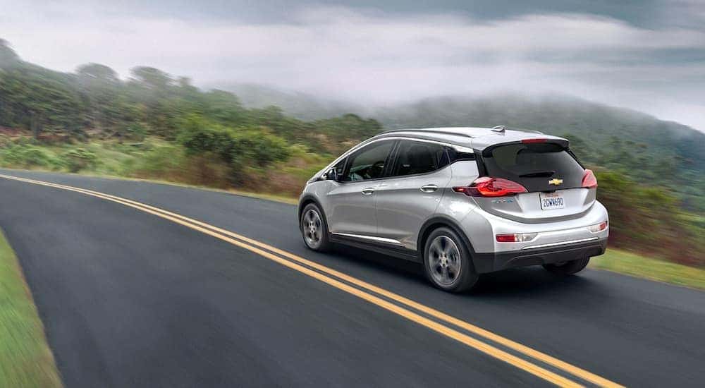 A silver 2020 Chevy Bolt EV is driving down a two way road after leaving a used Chevy dealership.
