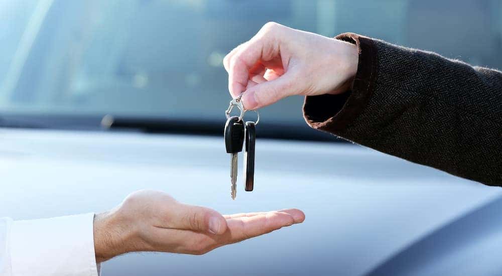 A salesman is passing a customer a set of keys at a used car dealer in Louisville.
