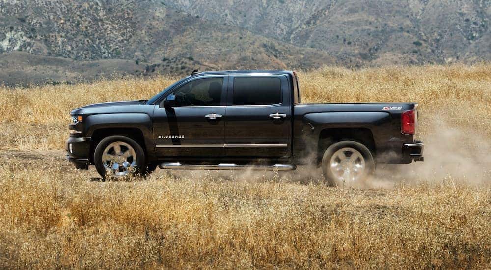 A black 2018 Chevy Silverado 1500 is shown driving through a hay field after leaving a used truck dealership.