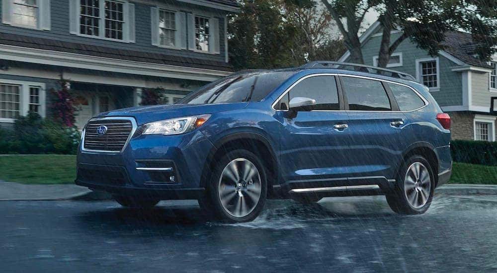 A blue 2020 Subaru Ascent is shown driving in the rain on a suburban street.