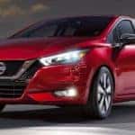 A red 2020 Nissan Versa is shown driving down a city street at night.