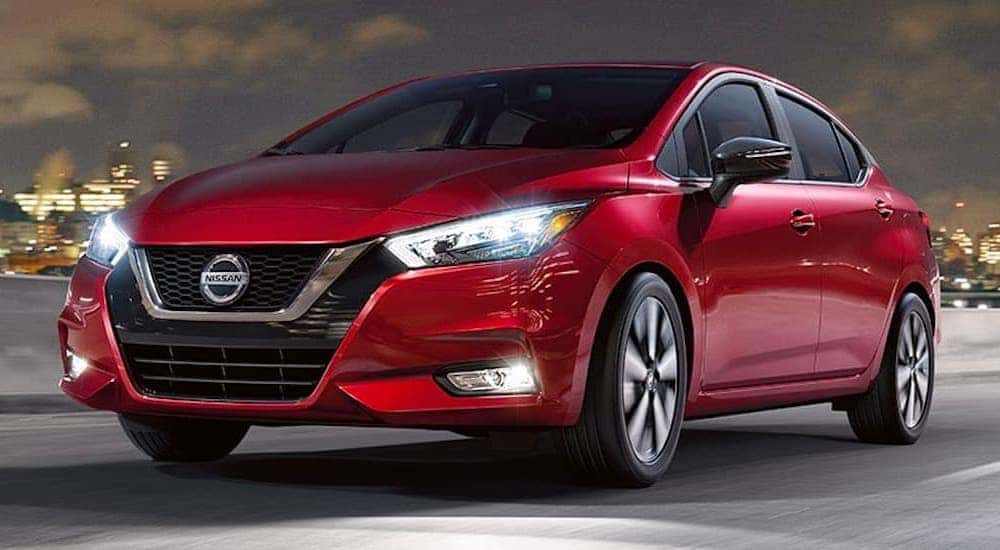 A red 2020 Nissan Versa is shown driving down a city street at night.