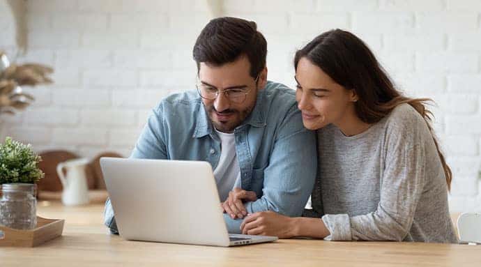 A couple sitting at kitchen table, shopping for vehicles on laptop.