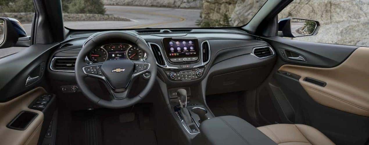 The black and tan interior of a 2022 Chevy Equinox shows the steering wheel and infotainment screen.