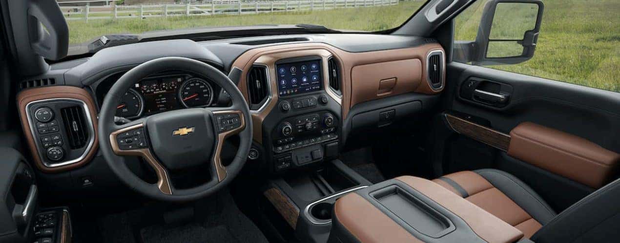 The black and tan interior of a 2022 Chevy Silverado 3500HD shows the steering wheel and infotainment screen.