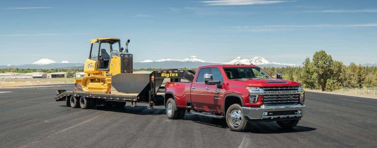 A red 2022 Chevy Silverado 3500HD is shown towing heavy machinery.