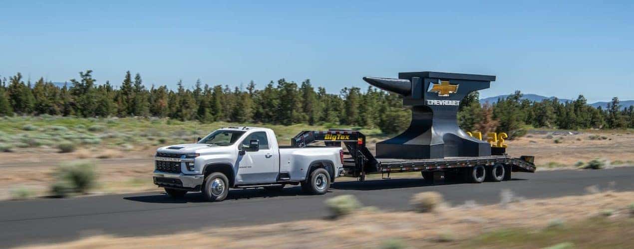 A white 2022 Chevy Silverado 3500HD is shown from the side towing a large anvil.