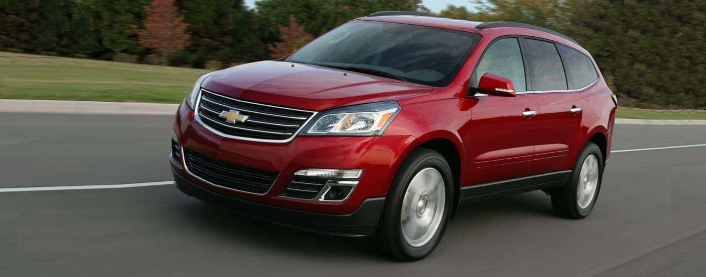 A red 2014 Chevy Traverse LTZ is shown driving past trees.