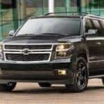 A black 2018 Chevy Suburban is shown parked in front of a modern building.