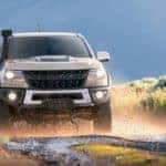 A tan 2022 Chevy Colorado ZR2 is shown from a front angle driving on a dirt road through a field.