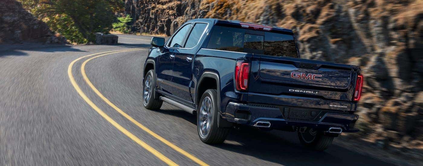 A black 2022 GMC 1500 Sierra Denali is shown from behind driving past a rock face.