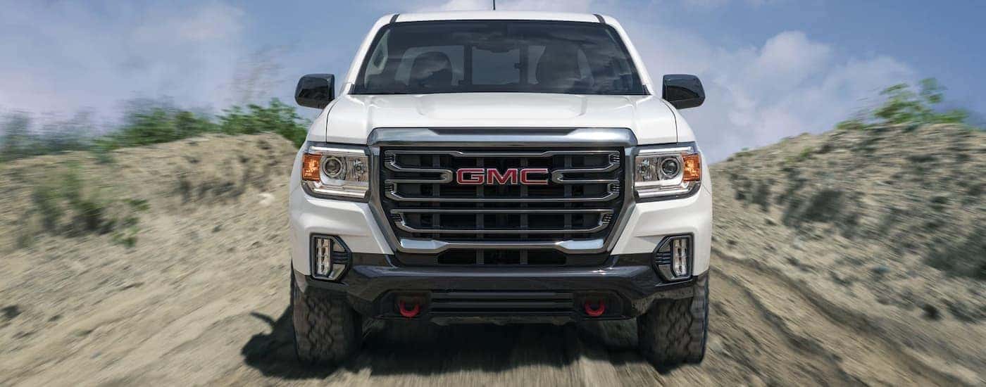 A white 2022 GMC Canyon AT4 is shown from the front speeding down a dirt path.