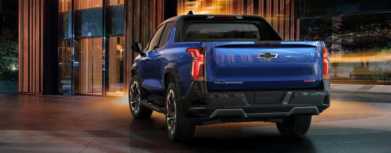 A blue 2024 Chevy Silverado EV RST is shown from a rear angle in a city.