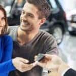 Car salesman giving the key of the new car to the young attractive owners