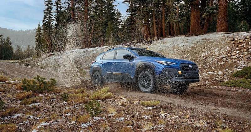 Blue 2026 Subaru Crosstrek SUV driving over muddy terrain.