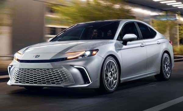 A silver 2026 Toyota Camry, in motion, driving downtown.