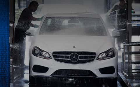 A white Mercedes-Benz going through a car wash with a man hand washing it.