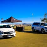 two white Mercedes-Benz vehicles parked on the grass in front of a pop-up tent